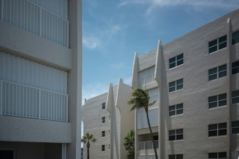 White condominium buildings with balconies and palm trees under a blue sky